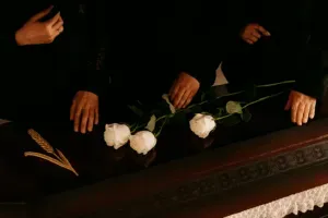 Mains de personnes en deuil posées sur un cercueil avec des roses blanches.