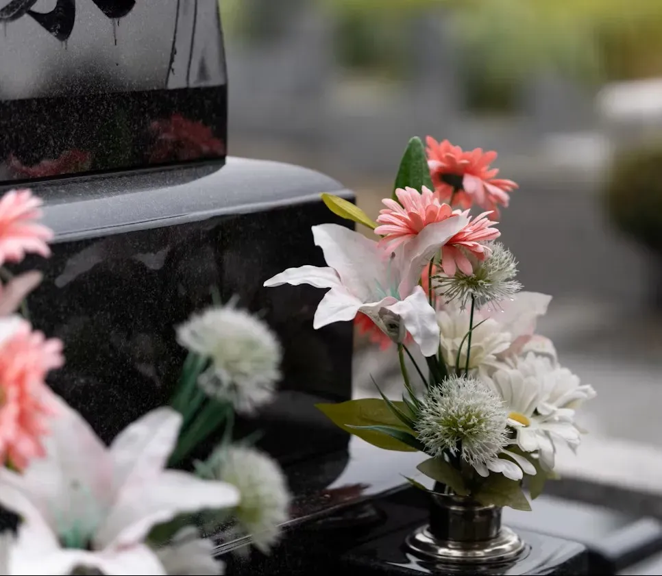Gros plan sur un bouquet de fleurs artificielles colorées posé sur une pierre tombale.