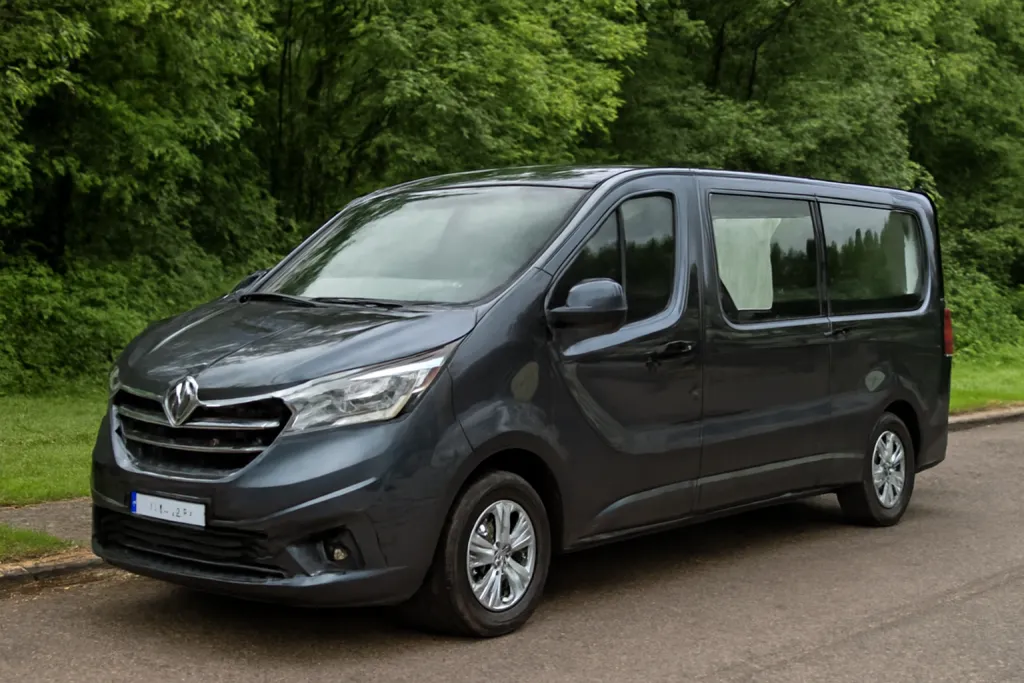 Fourgon corbillard Renault Trafic de couleur gris foncé stationné au bord d'une route arborée.