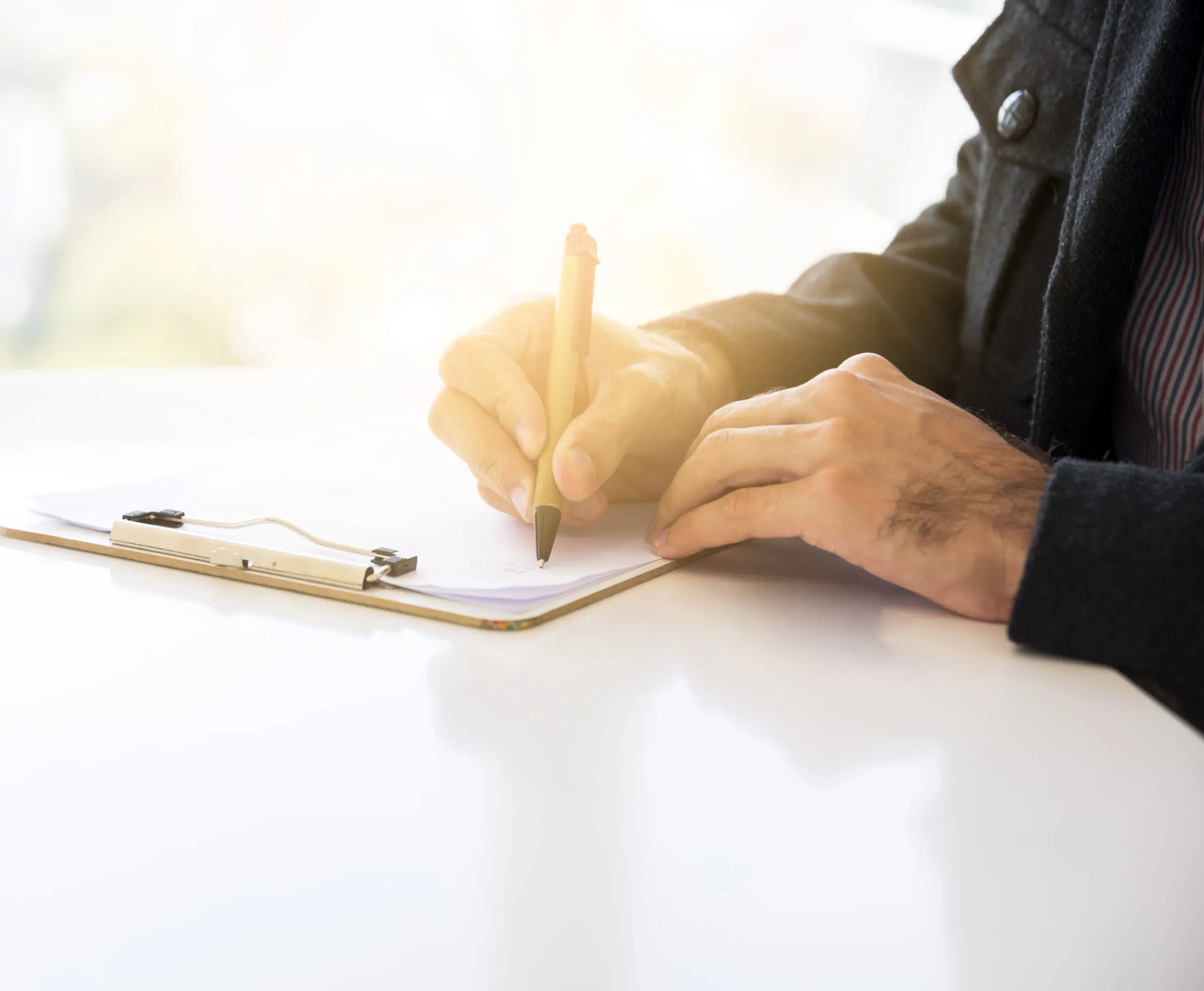 Gros plan sur un homme signant un document sur un porte-bloc à son bureau.